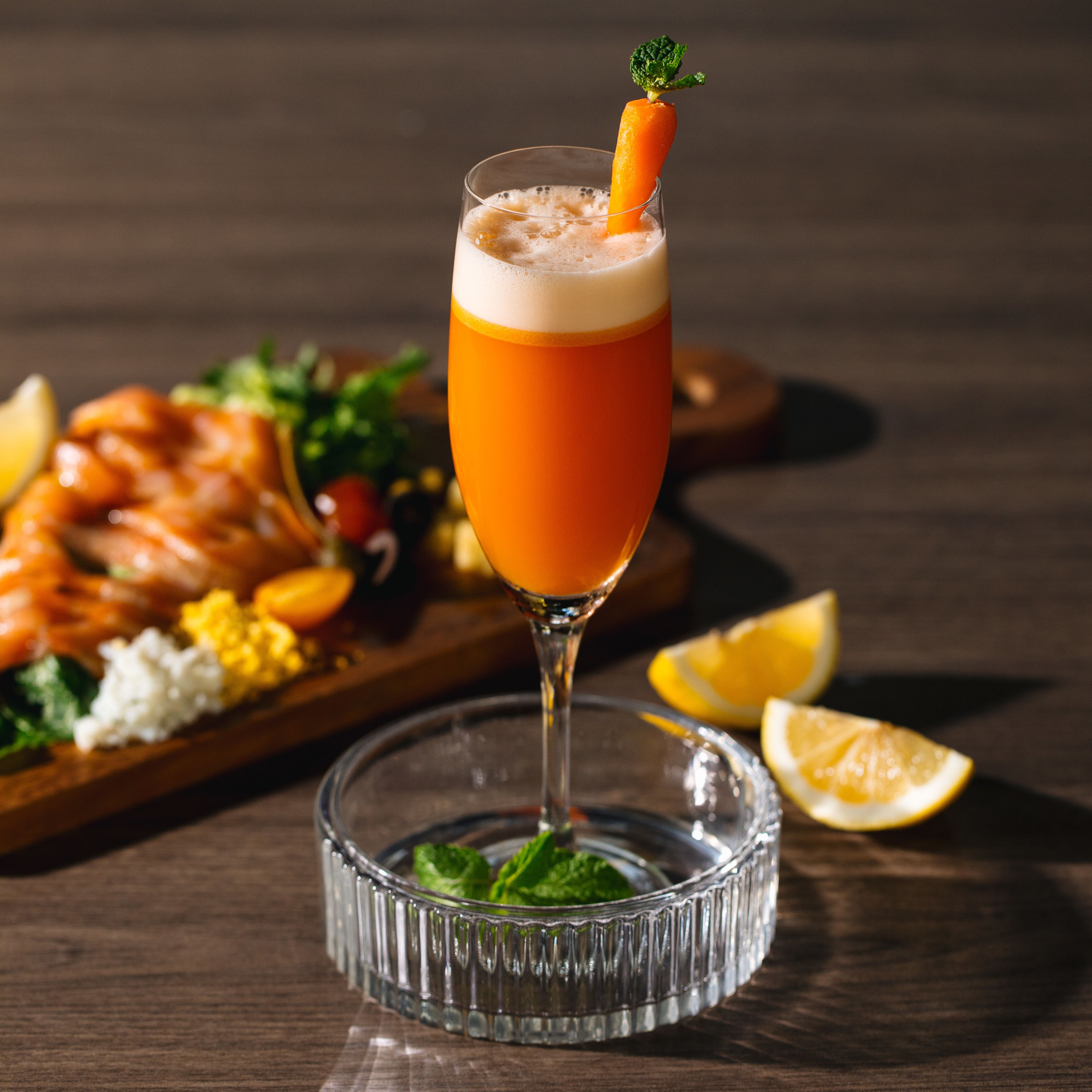 Ein Glas Orangensaft mit einer Karotten-Garnitur auf einem Holztisch.