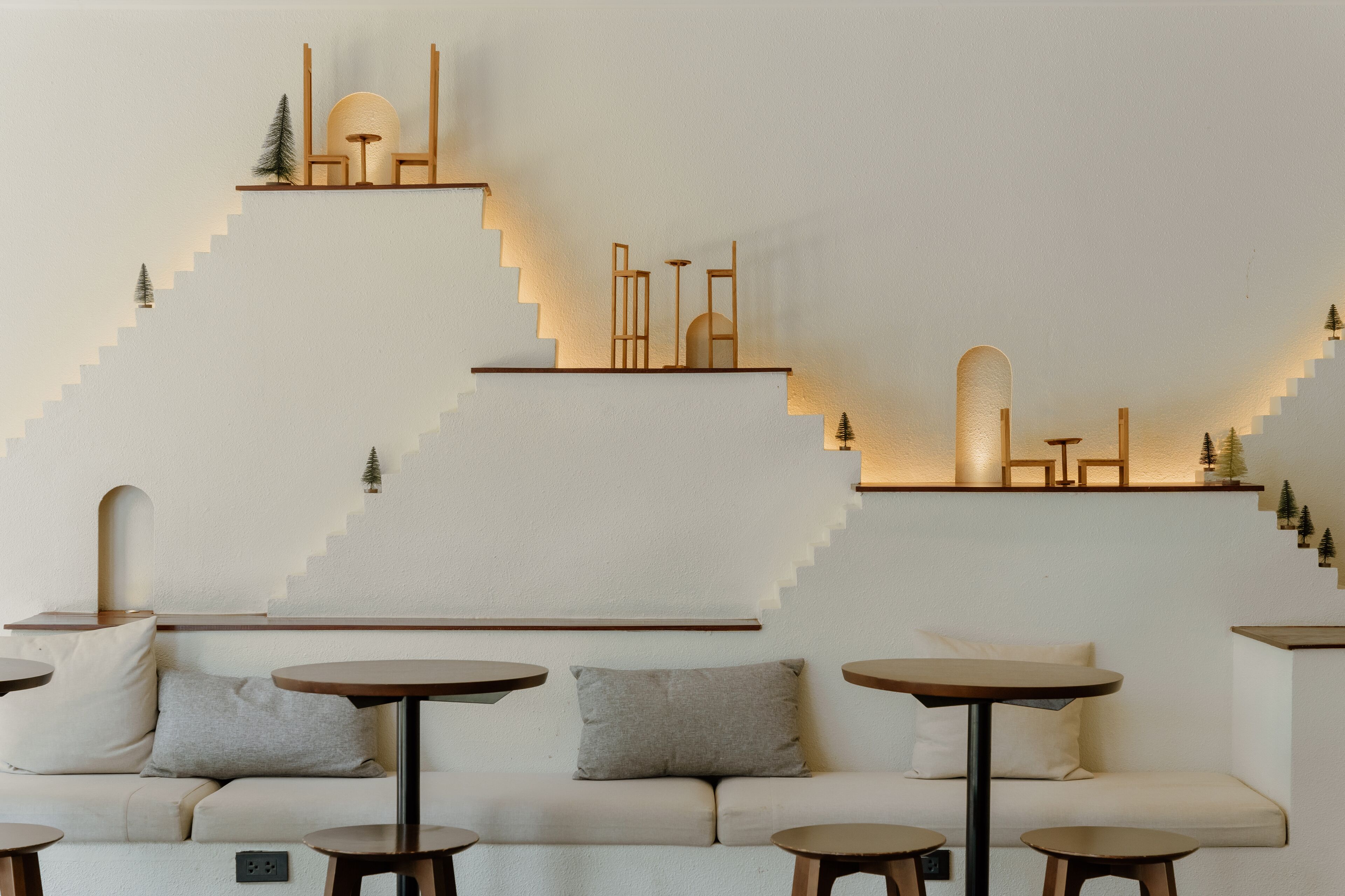 A modern interior with a sofa and round tables, a staircase with geometric wall art, and a minimalist design.