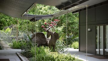 A garden area with a sculpture of a swan and red flowers, a pathway, and a building entrance.