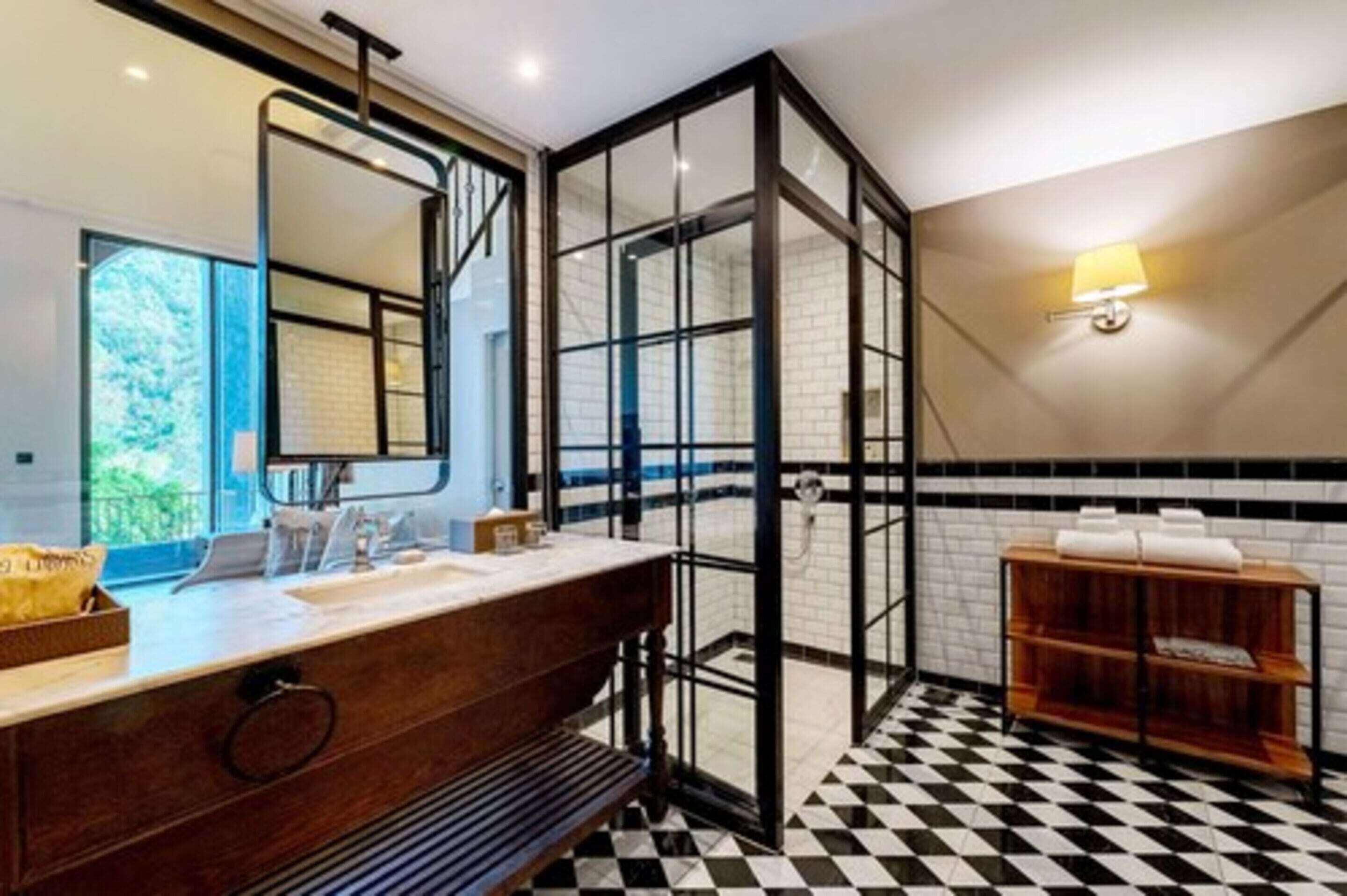 A modern bathroom with a large mirror, a wooden vanity, a black and white checkered floor, and a glass partition.