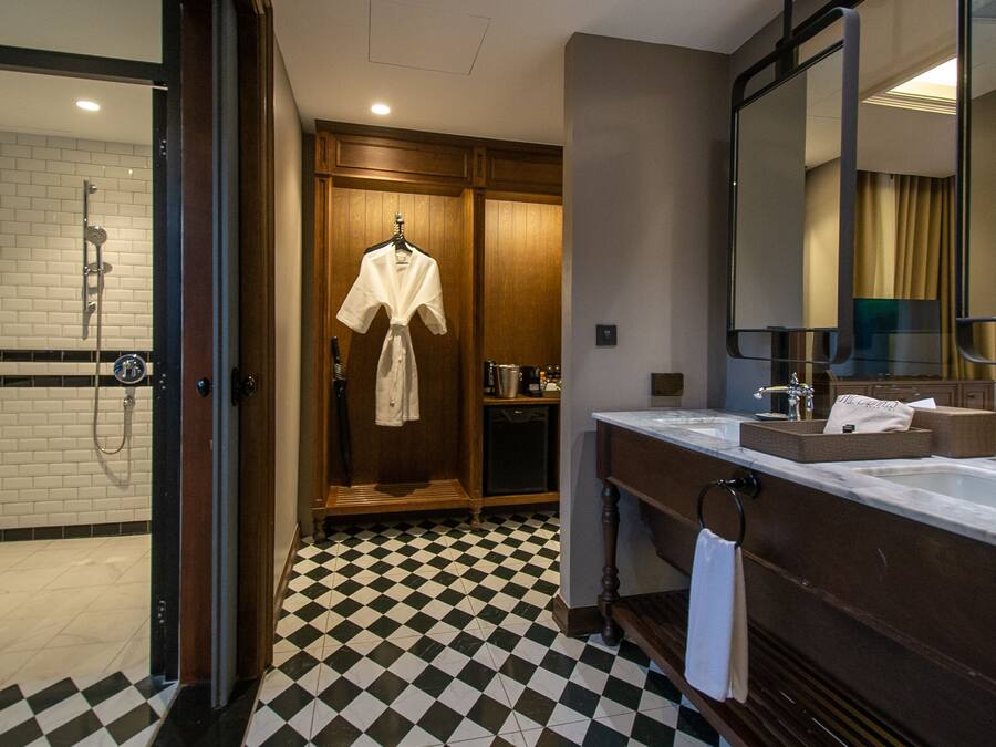 A hotel bathroom with a checkered floor, a shower, a robe hanging, a sink, and a mirror.