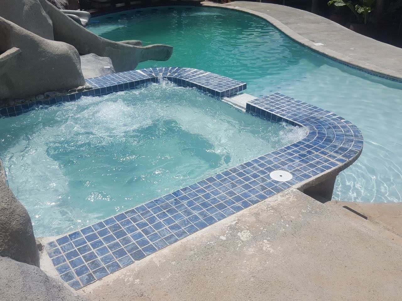 A swimming pool with a tiled hot tub area and a slide.