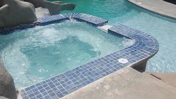 A swimming pool with a tiled hot tub area and a slide.