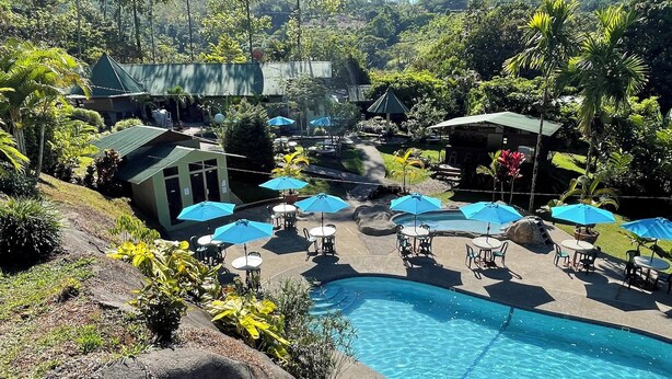 A pool area with lounge chairs and umbrellas, surrounded by greenery and a small building. - La Cantera Resort (Cajón)
