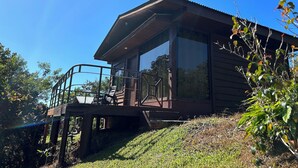 A wooden cabin with a balcony and large windows, surrounded by greenery. - La Cantera Resort (Cajón)