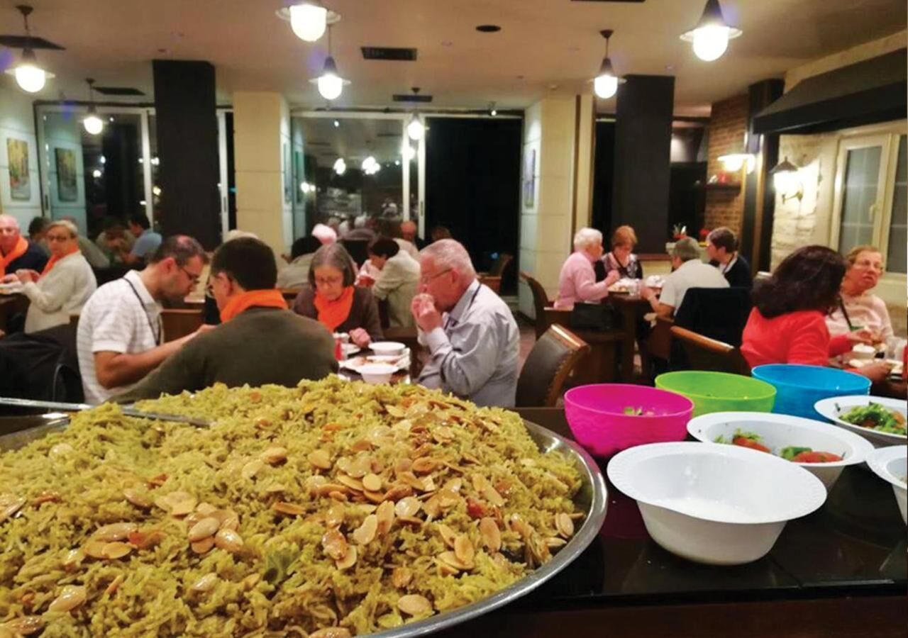 A buffet with a large serving of rice dishes, surrounded by people dining.