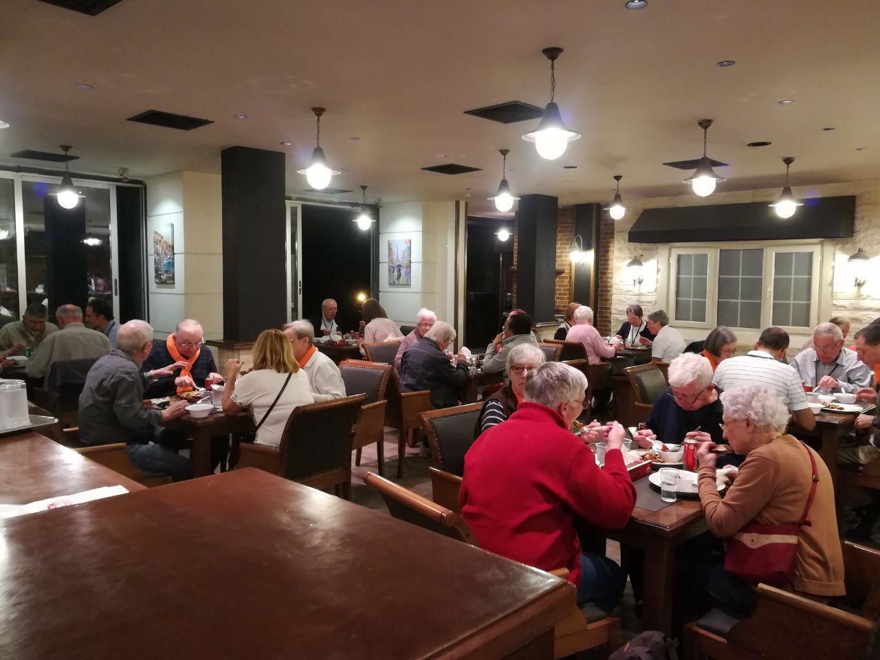 A dining area with multiple tables and chairs, people seated and eating.