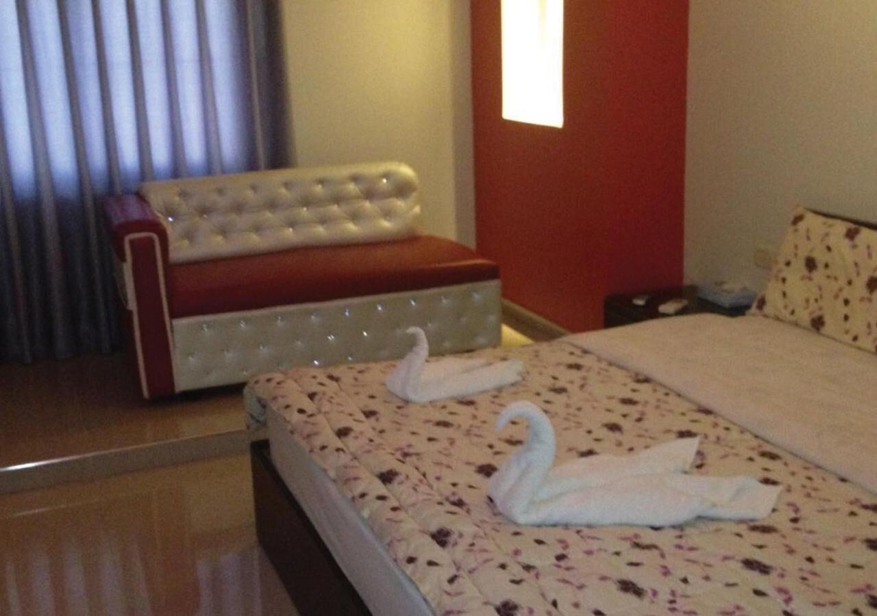 A hotel room with a bed, a red upholstered bench, and a window with blinds.