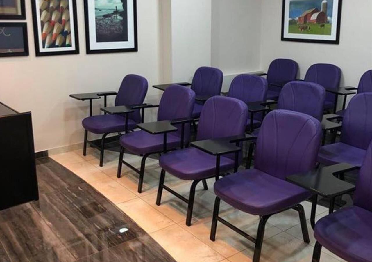 A conference room with rows of purple chairs and black tables, framed pictures on the wall, and a wooden floor.