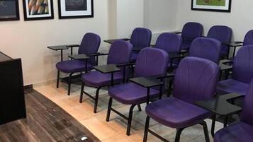 A conference room with rows of purple chairs and black tables, framed pictures on the wall, and a wooden floor.