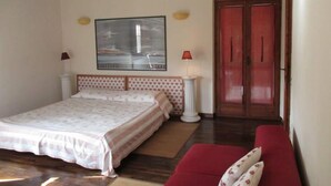 Un dormitorio con una cama, un sofá rojo, una puerta de madera y un cuadro enmarcado en la pared.