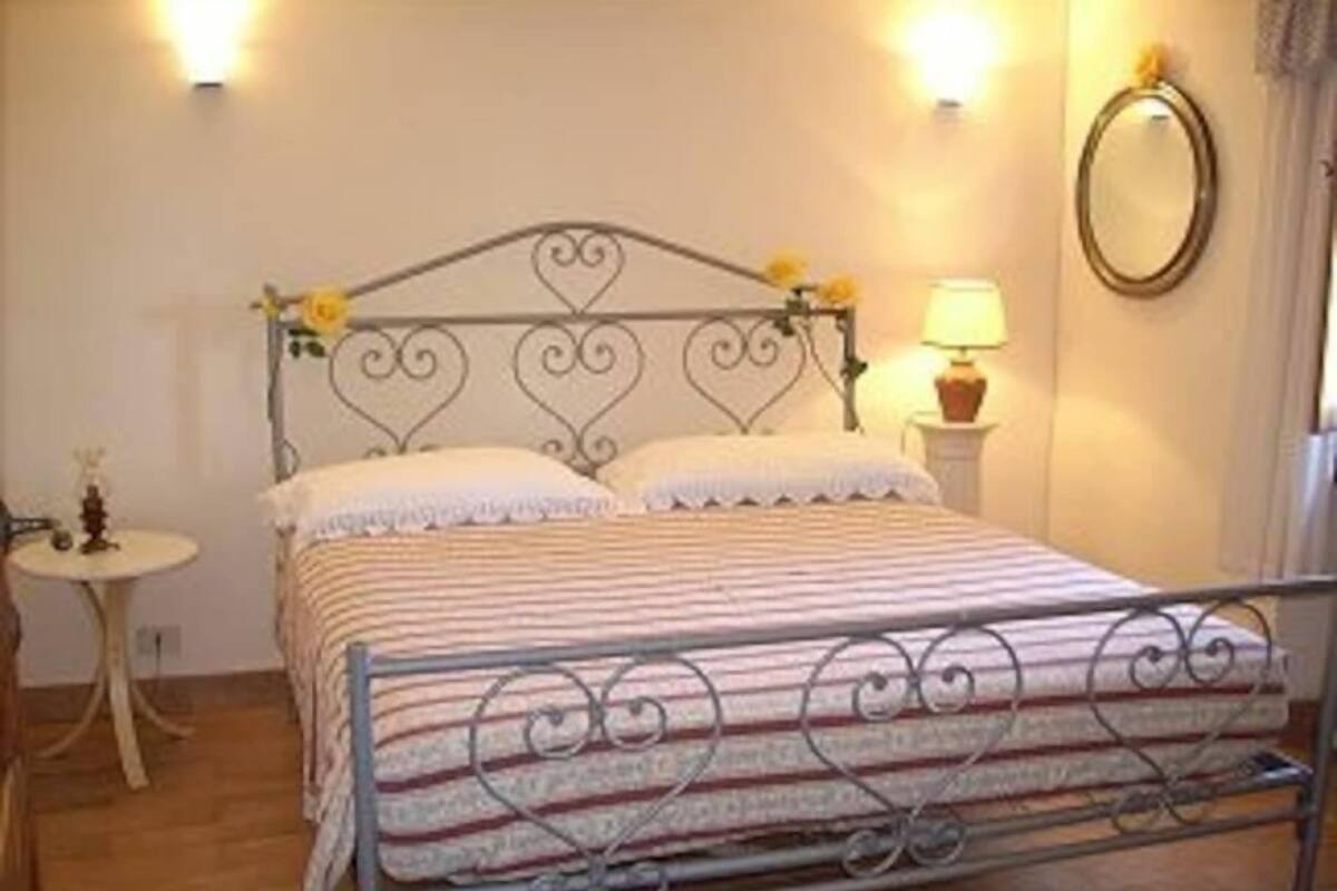 A bed with a metal frame and heart-shaped designs, a bedside table with a lamp, and a wall-mounted mirror.
