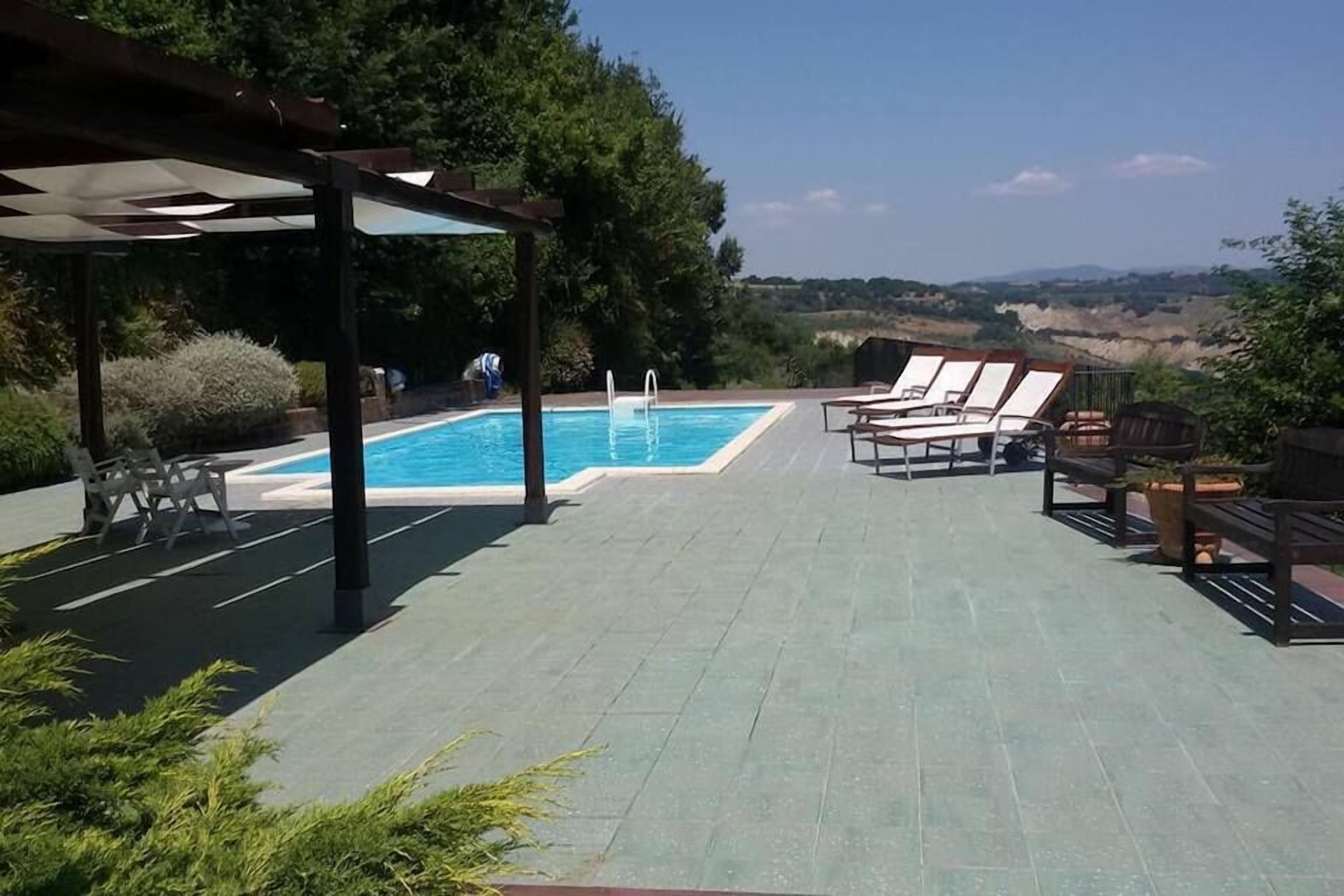 A poolside area with a covered seating area, a pool, and a view of the landscape.