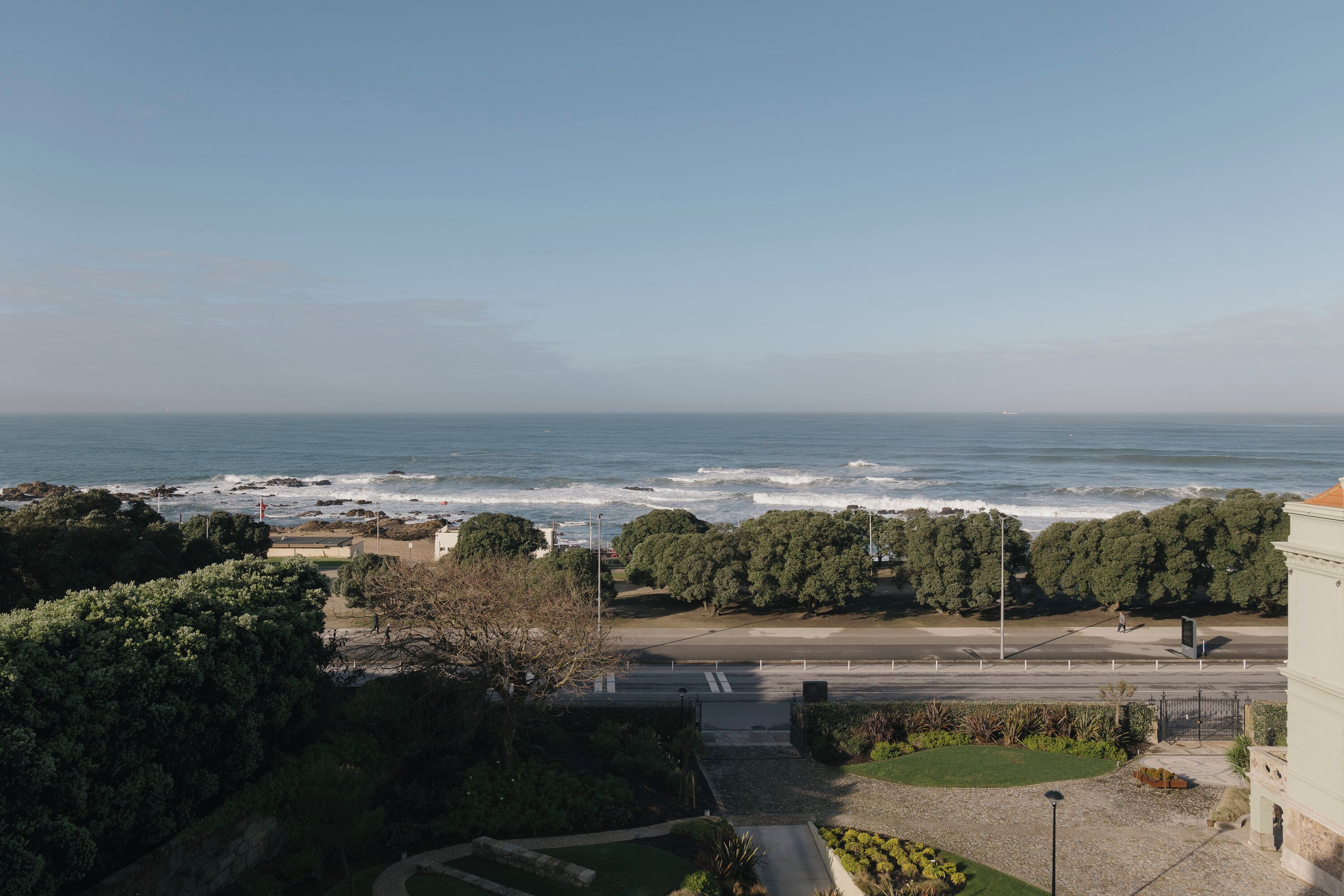 A coastal view with a beach, trees, and a road leading to a building.
