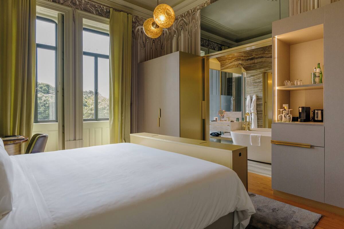 Hotellihuone, jossa on suuri sänky, peilillä varustettu meikkipöytä, pesuallas ja vaatekaappi.