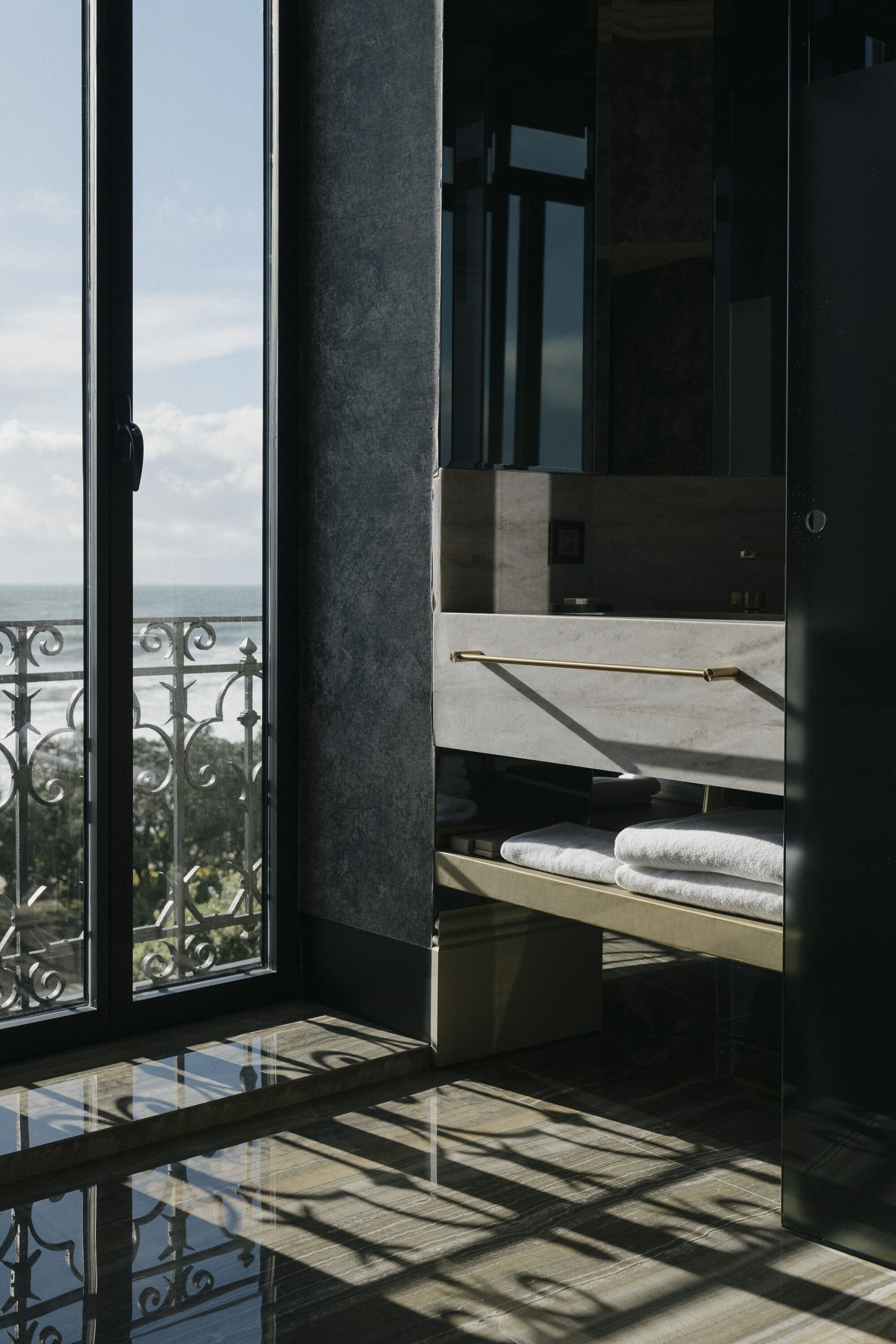 Een moderne badkamer met een douchecabine van glas, een handdoekhouder en uitzicht op zee door een balkondeur.