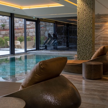 A modern indoor pool area with a stone wall, seating, and a view of the outside.