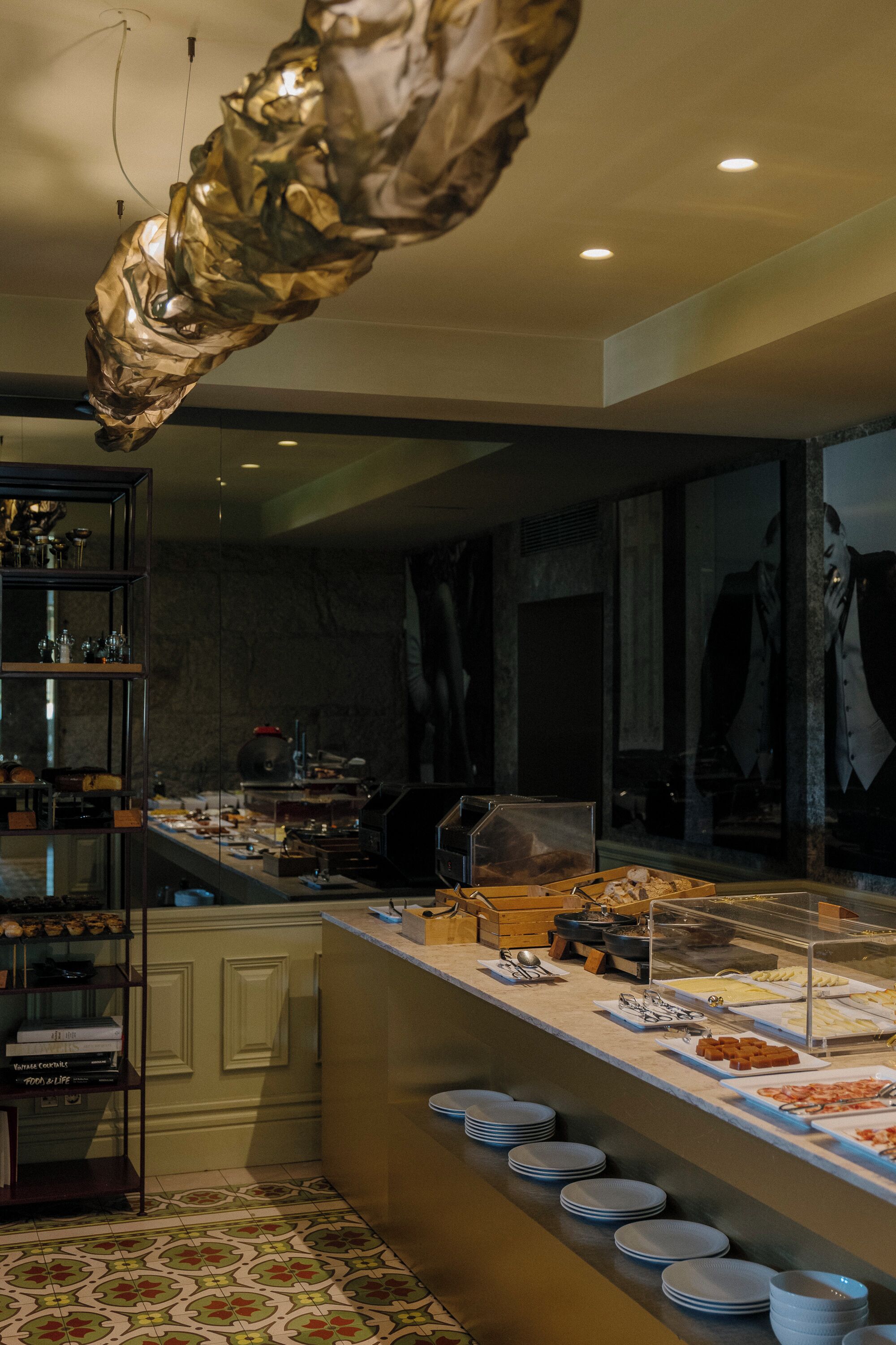 Uma área de buffet com diversos tipos de comida, um expositor de vidro e uma escultura pendente decorativa.