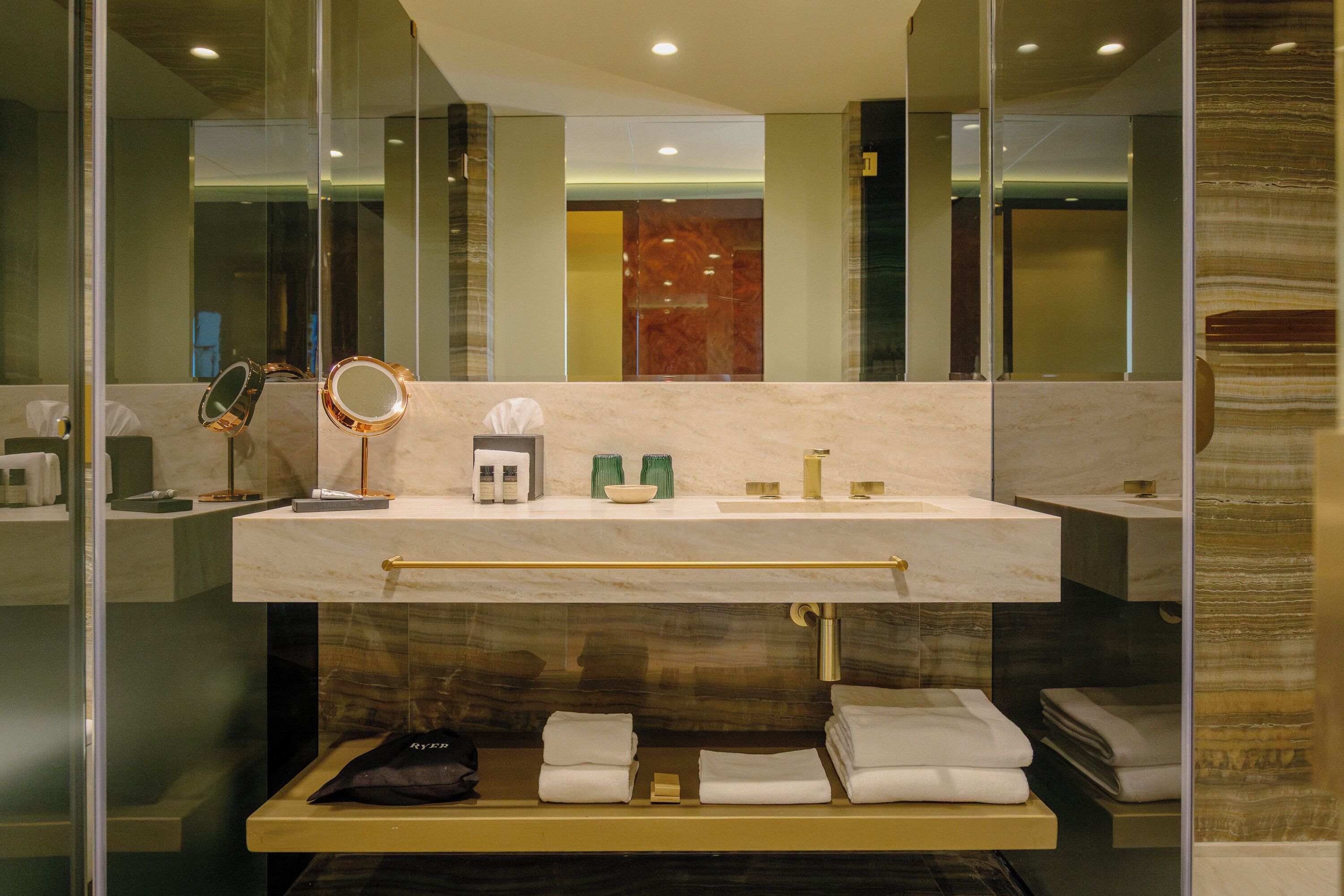 A modern bathroom with a large mirror, a vanity with a marble countertop, and neatly folded towels on a shelf.