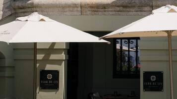 Un área de estar al aire libre con mesas y sillas, sombrillas, y fachada de edificio con detalles de piedra y letrero que dice "Flor de Lis Restaurant".