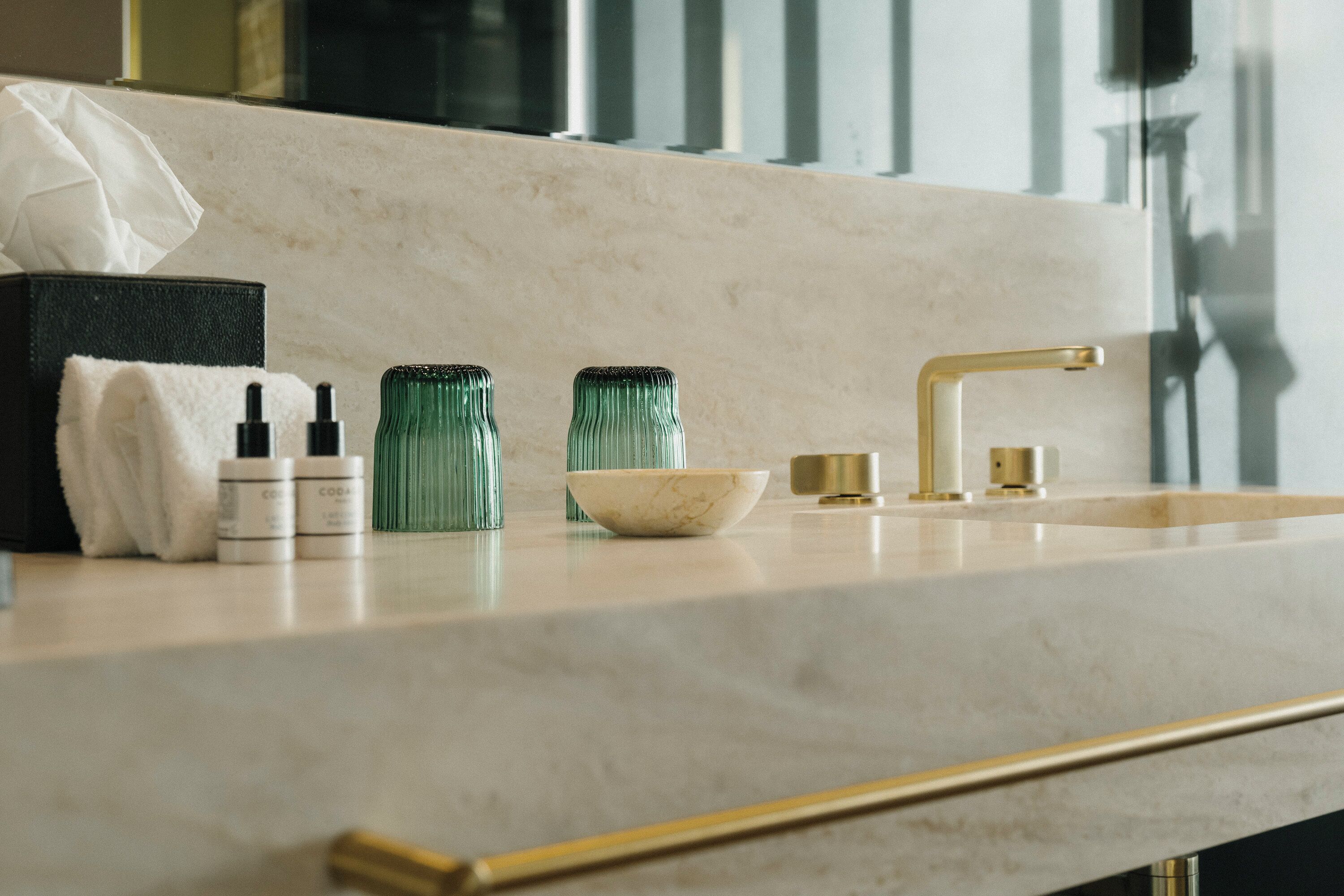 A bathroom vanity with a marble countertop, a gold faucet, and two green glass bottles.