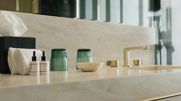 A bathroom vanity with a marble countertop, a gold faucet, and two green glass bottles.
