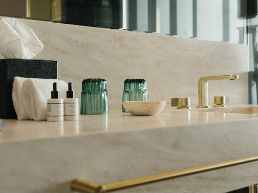 A bathroom vanity with a marble countertop, a gold faucet, and two green glass bottles.