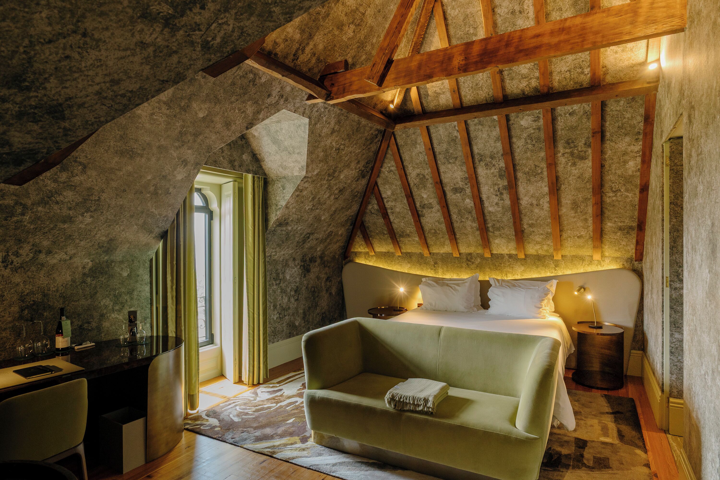 A cozy attic bedroom with a sloped ceiling, a green sofa, a bed, and a desk with a chair.