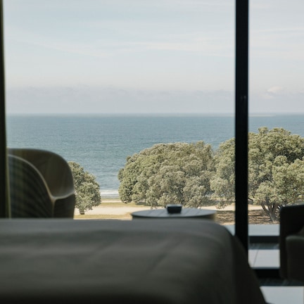 A room with a view of the sea and trees through large windows.