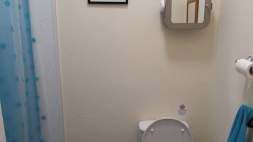 Une petite salle de bain comprenant des toilettes, un lavabo, un rideau de douche, un tableau encadré et une plante en pot.