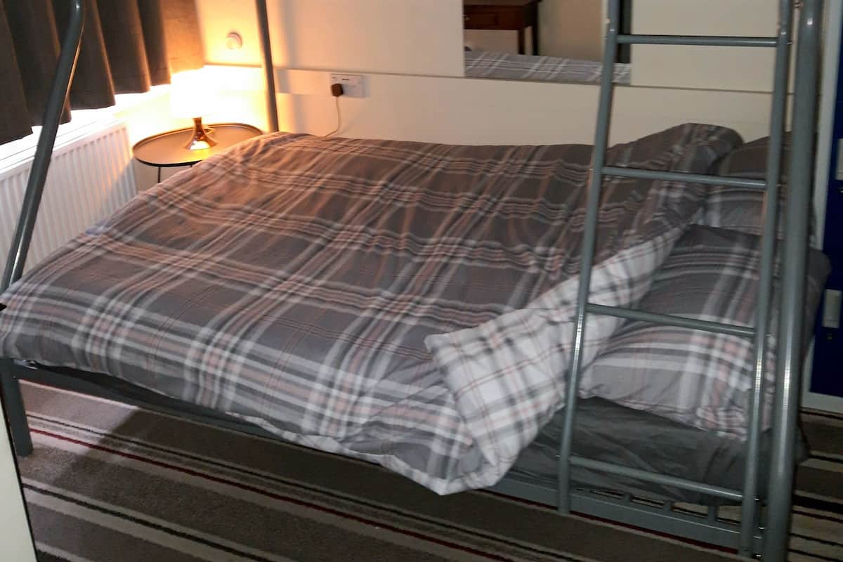 Un lit superposé avec une couverture à carreaux et des oreillers, une lampe et un tableau encadré accroché au mur.