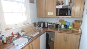 A compact kitchen with wooden cabinets, a microwave, a toaster, and a sink. - Hull Trinity Backpackers (Hull)