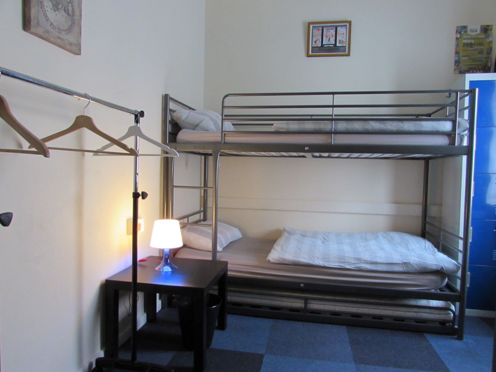 A bunk bed room with a desk and lamp, a framed picture on the wall, and a blue cabinet.