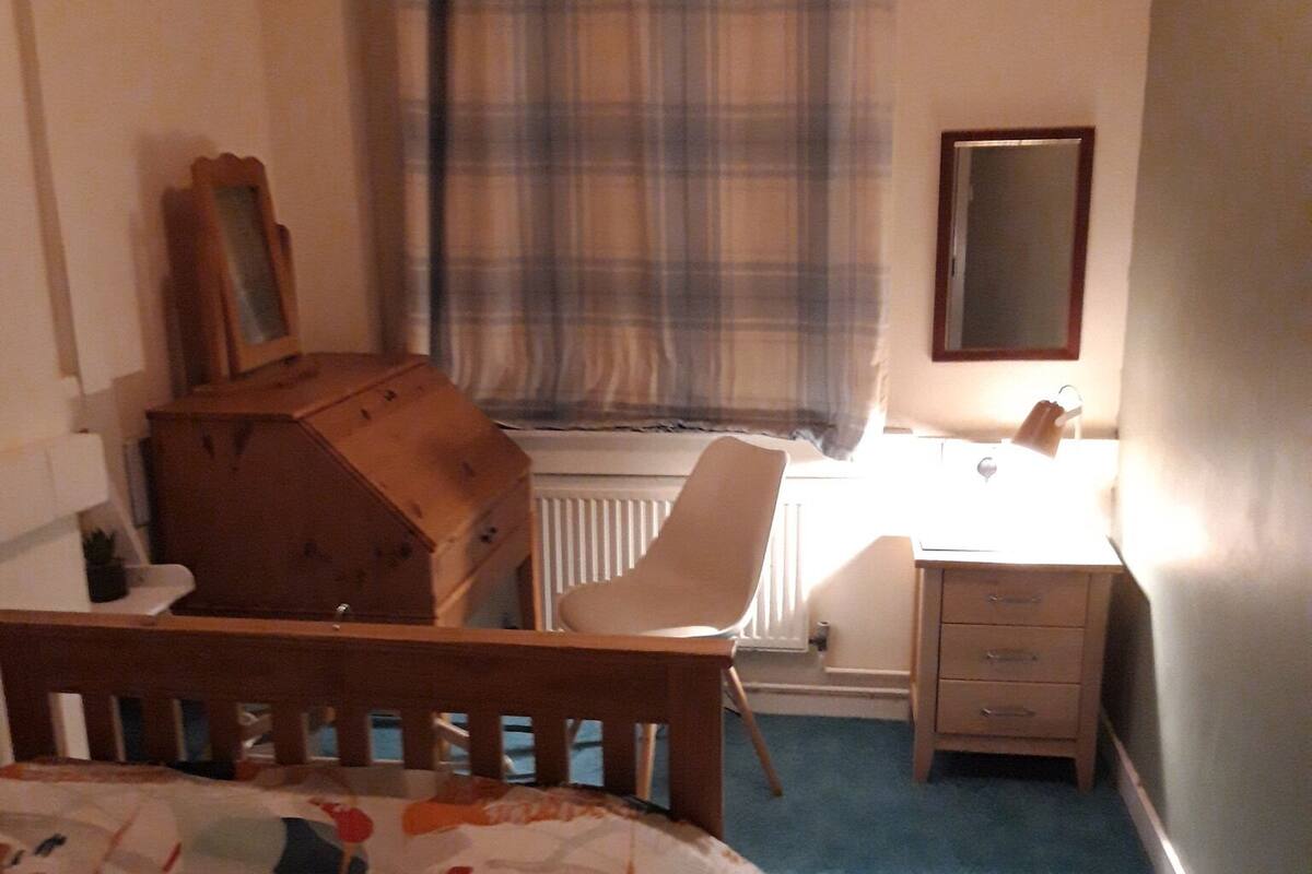 Une chambre à coucher comprenant un lit, une chaise, un bureau, une commode, un radiateur et un miroir.