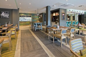 A modern restaurant interior with multiple dining tables and chairs, a kitchen area, and a bar.