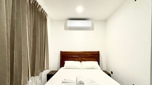 A neatly made bed with a wooden headboard, white bedding, and a rolled towel on the foot of the bed. There is a ceiling-mounted air conditioning unit above the bed. - Pura Natura Lodge (Quepos)