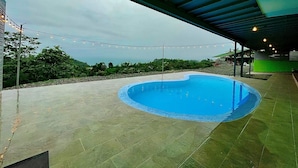 A swimming pool with a curved edge, surrounded by a paved area. - Pura Natura Lodge (Quepos)