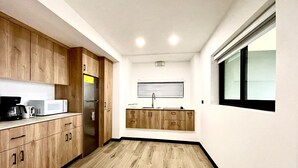 A compact kitchen with wooden cabinets, a built-in microwave, and a refrigerator. - Pura Natura Lodge (Quepos)