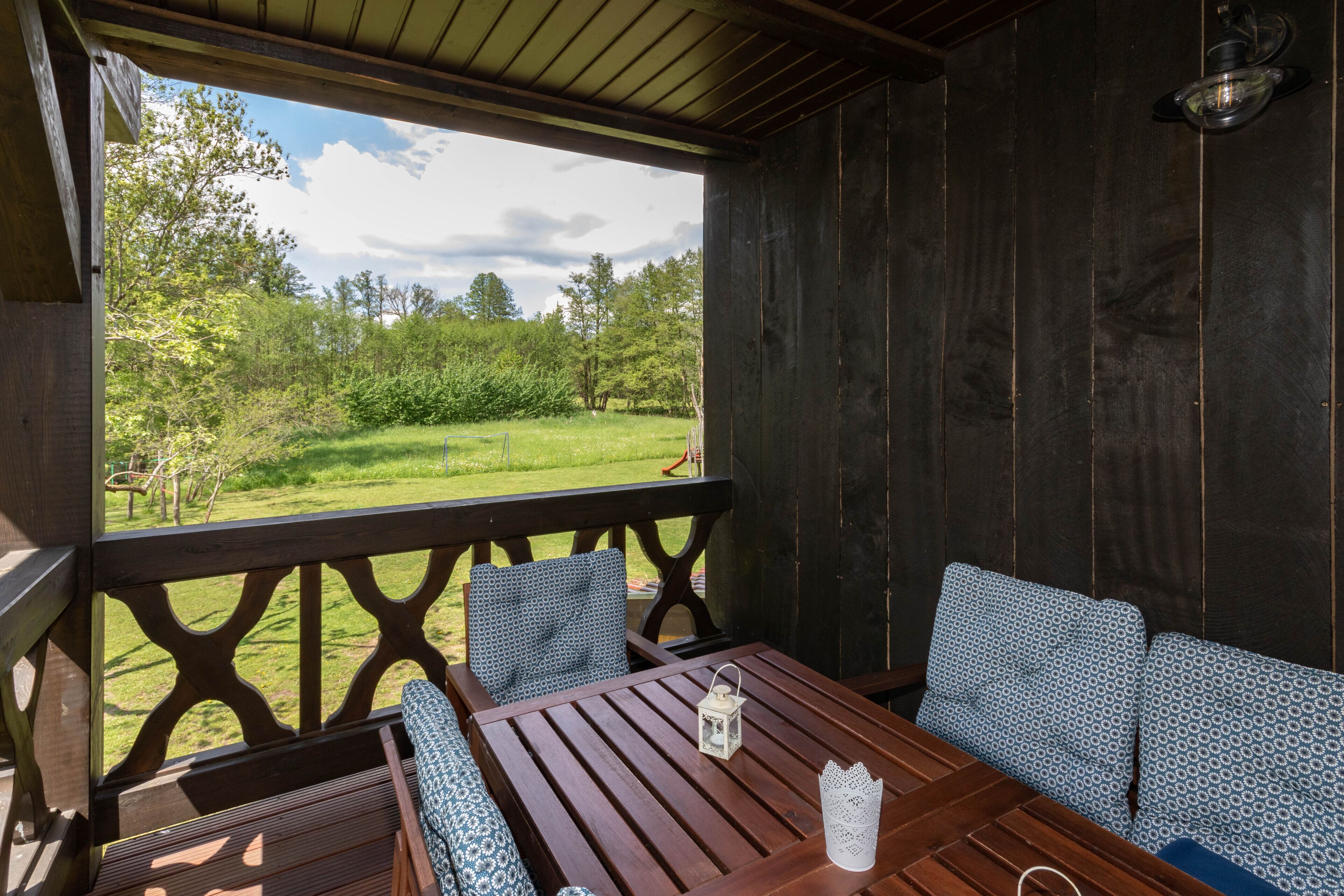 A wooden deck with a table and chairs, overlooking a grassy area with trees.