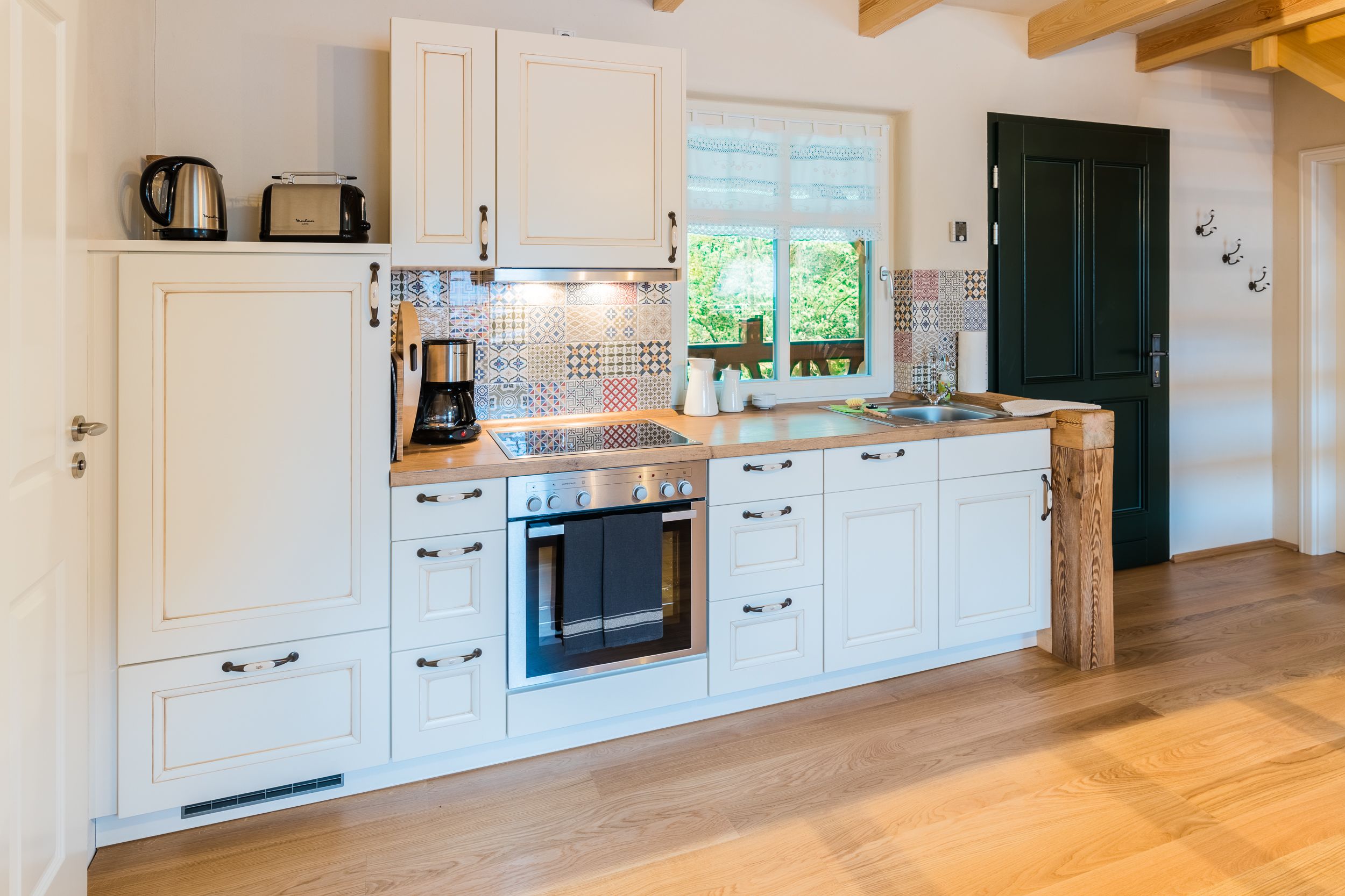 A kitchen with white cabinets, a built-in oven, a coffee maker, and a window with a view of greenery.
