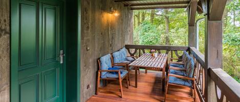 Une terrasse en bois avec une porte verte, une table et quatre chaises à motifs bleus.
