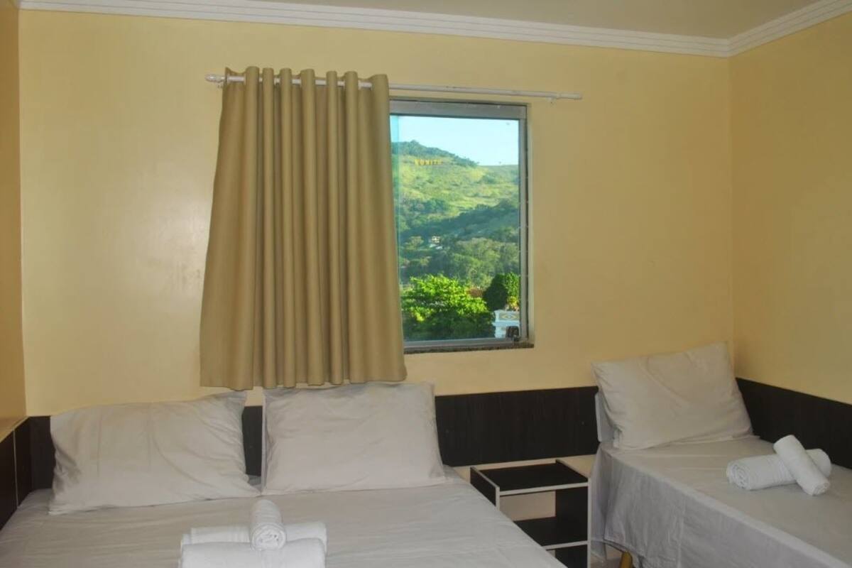Habitación de hotel con dos camas, una ventana con cortinas y vistas a un paisaje verde.