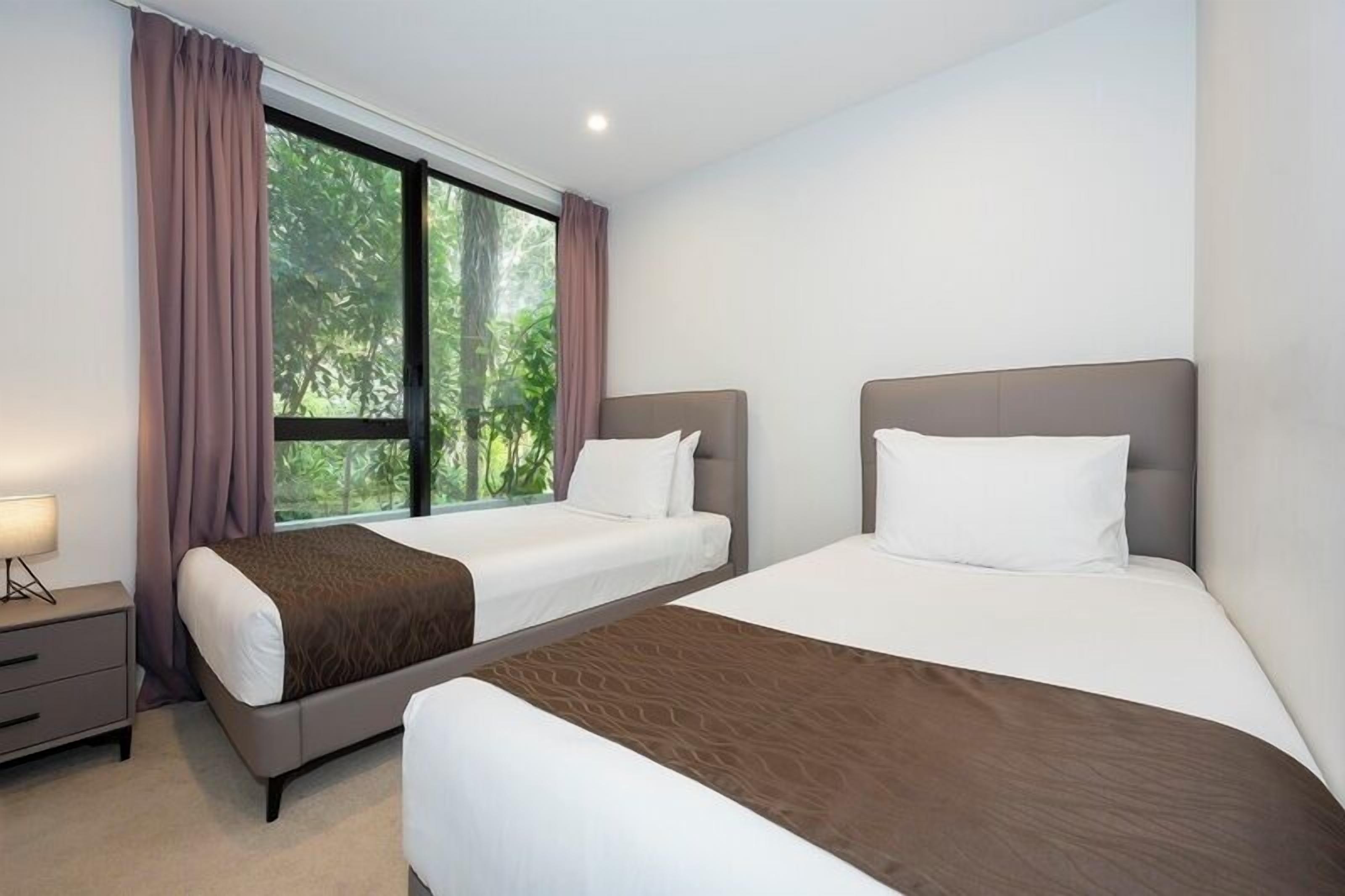 A hotel room with two beds, a nightstand, and a window with curtains.