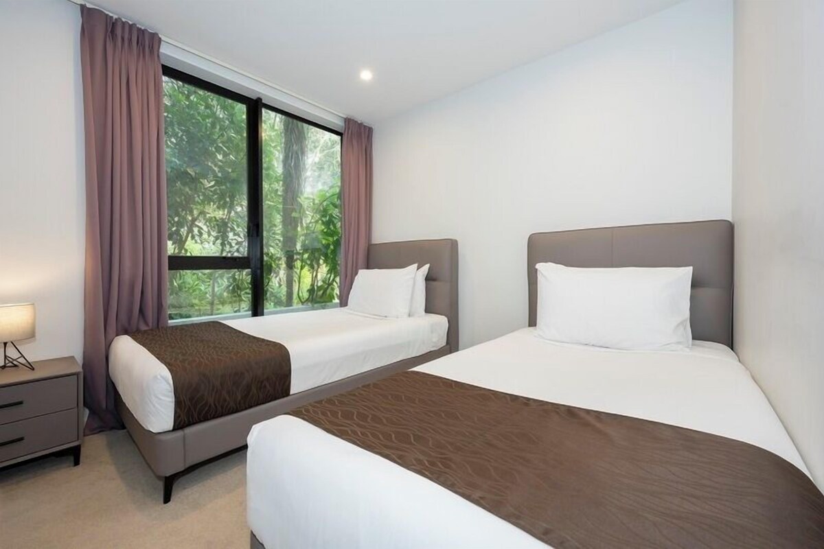 A hotel room with two beds, a nightstand, and a window with curtains.