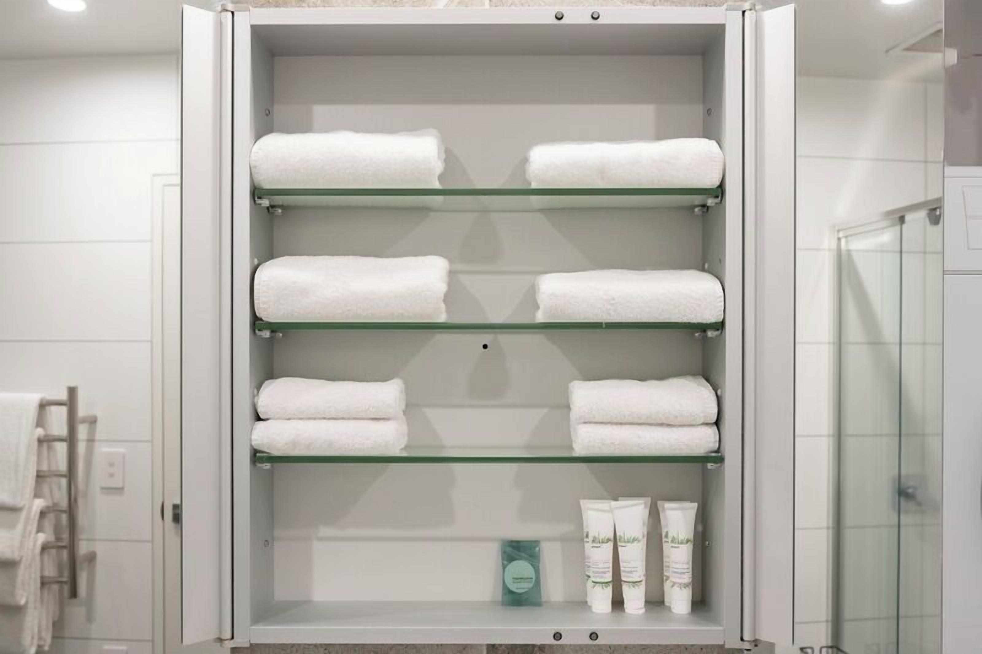 A bathroom with a glass-fronted cabinet holding white towels and toiletries.