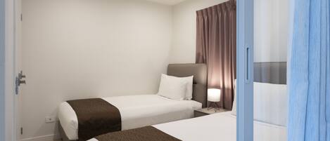 A hotel room with two beds, a nightstand, a lamp, and a window with curtains.
