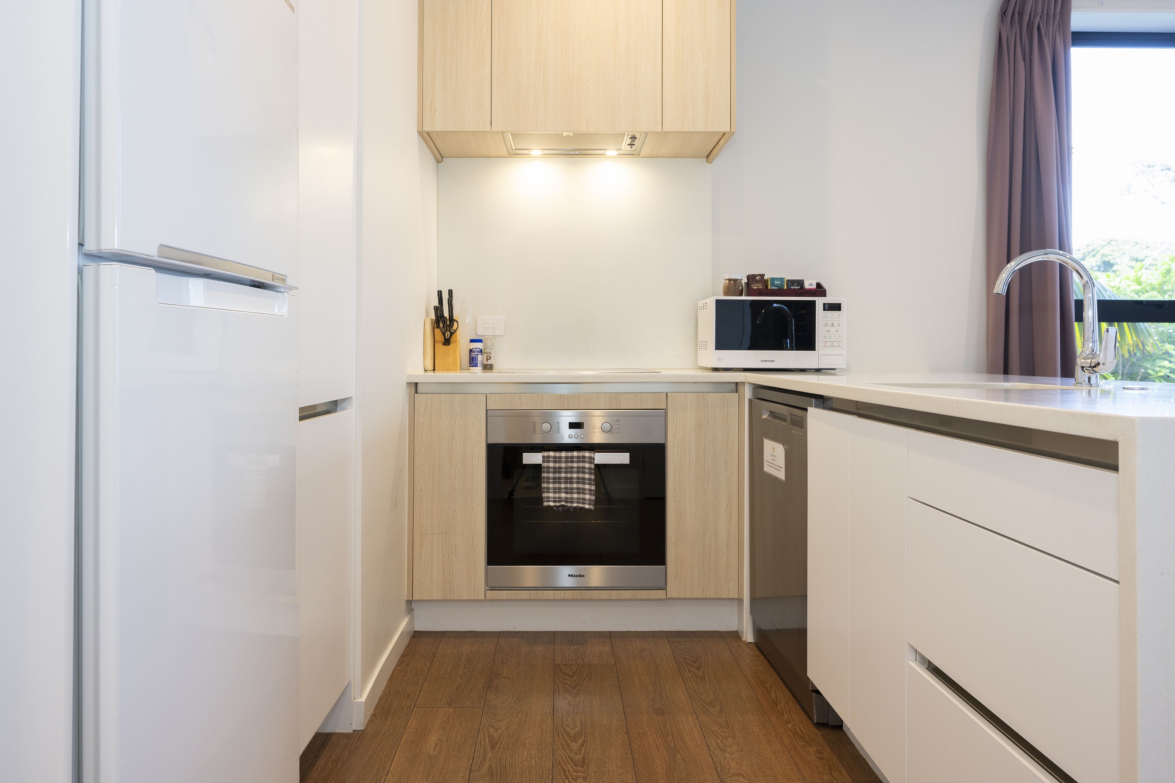 A compact kitchen with a built-in oven, microwave, and stainless steel refrigerator.