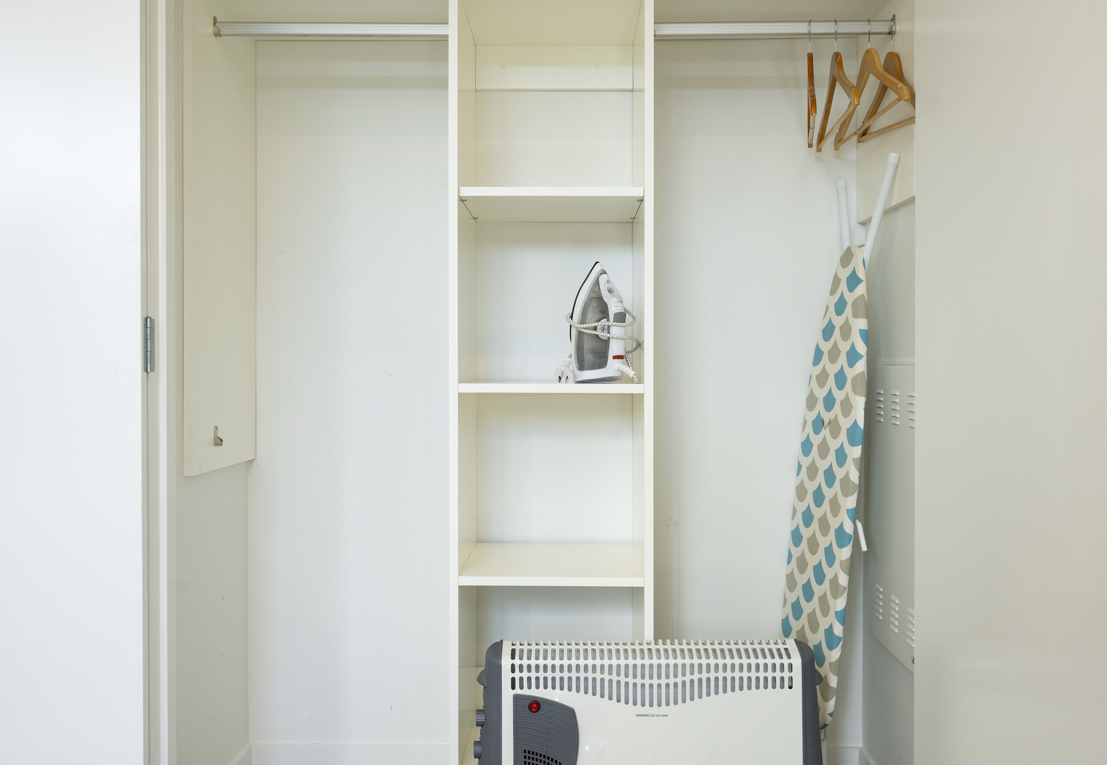 Ein weißer Kleiderschrank mit Einlegeböden, einem Bügeleisen und Kleiderbügeln.