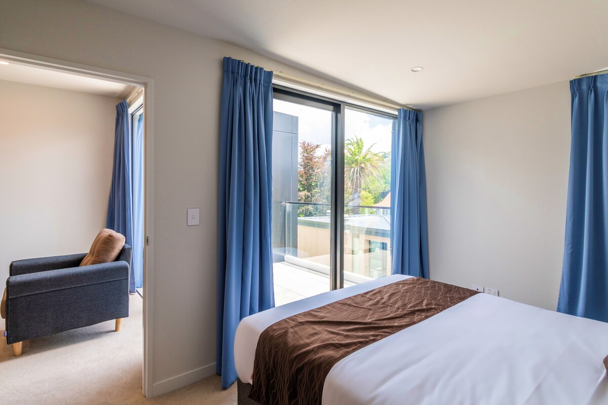 A hotel room with a bed, a seating area, and a balcony with curtains.