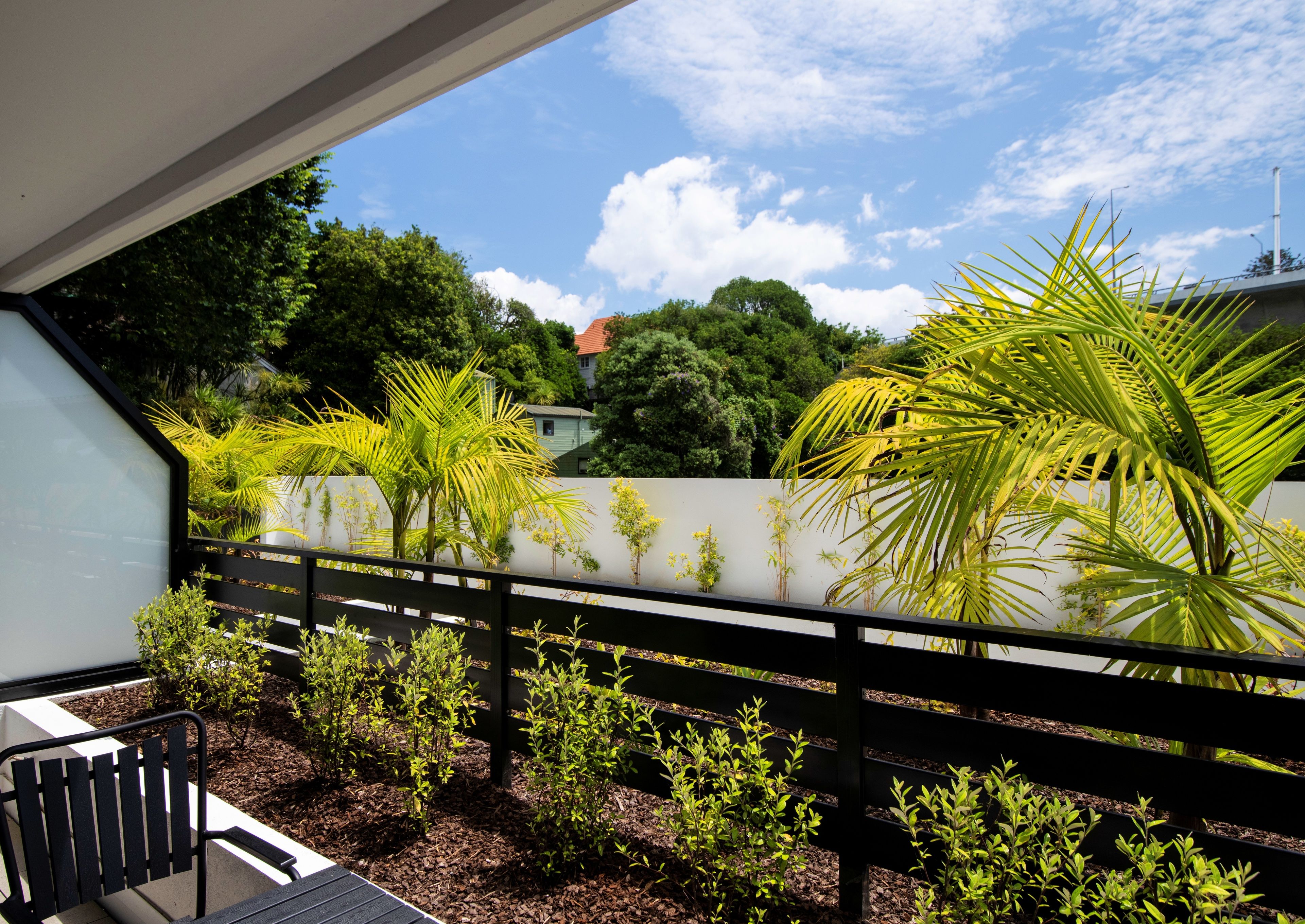A balcony with a black railing, potted plants, and a view of a residential area with trees and a house.